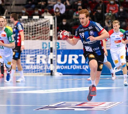 Ein Handball-Spieler läuft mit dem Handball in der Hand vorweg. Weitere Spieler folgen ihm. 