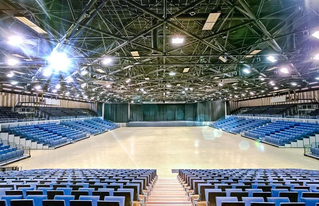 Blick durch den leeren Innenraum auf die Bühne. Rechts und links sieht man die blauen Sitze auf den Rängen. 