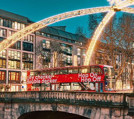 Weihnachtliche Installation in der Düsseldorfer Innenstadt: Brücke über den Kö-Graben mit einem roten Doppeldecker-Bus, der unter dem Lichterdom über die Brücke fährt  