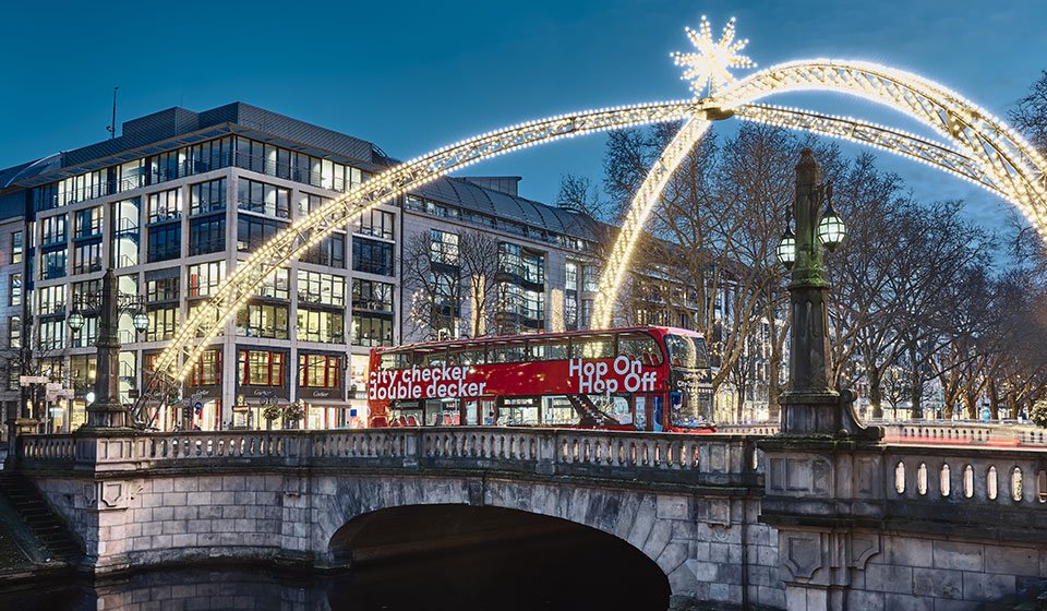Weihnachtliche Installation in der Düsseldorfer Innenstadt: Brücke über den Kö-Graben mit einem roten Doppeldecker-Bus, der unter dem Lichterdom über die Brücke fährt  