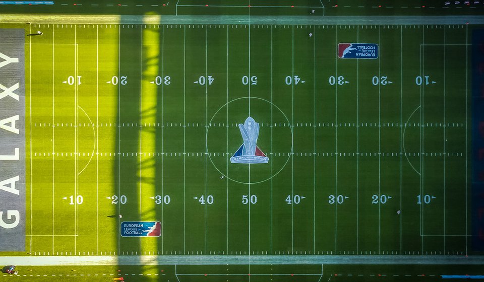 Drohnenaufnahme vom Football-Feld. In der Mitte des Feldes sieht man einen Pokal abgebildet, an den Rändern sind jeweils das Logo der European Football League. 